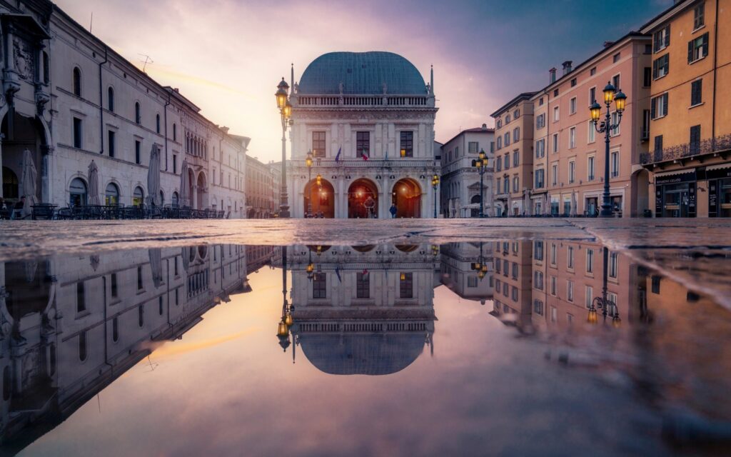a view of Brescia, Italy at sunset with the building reflecting off of water